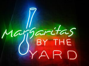 A neon sign that says margaritas by the yard.