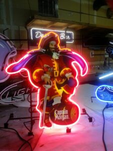 A neon sign of captain morgan in front of some other signs